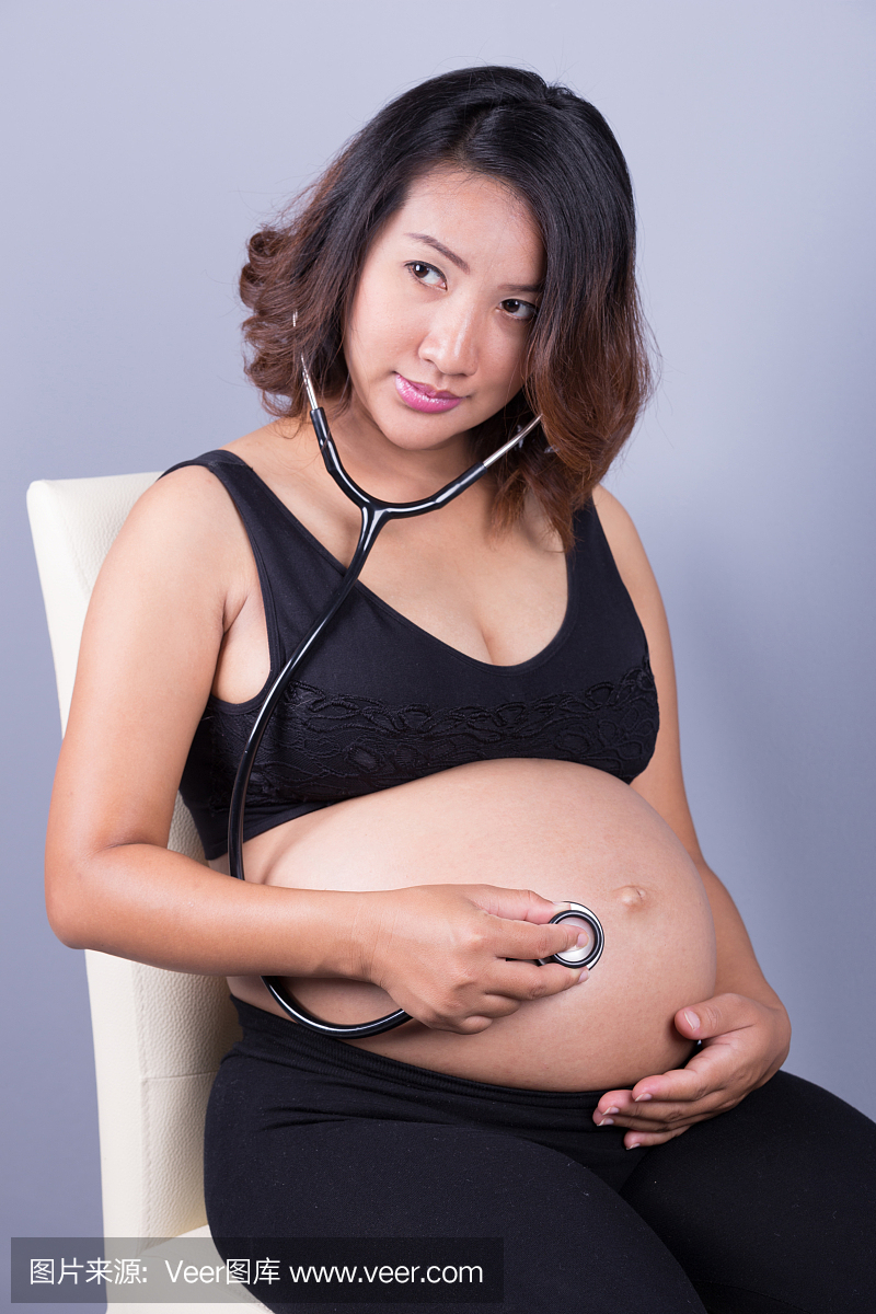 年轻怀孕的亚裔妇女用听诊器听肚子