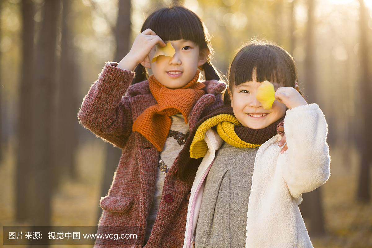 两个小女孩用树叶遮住眼睛