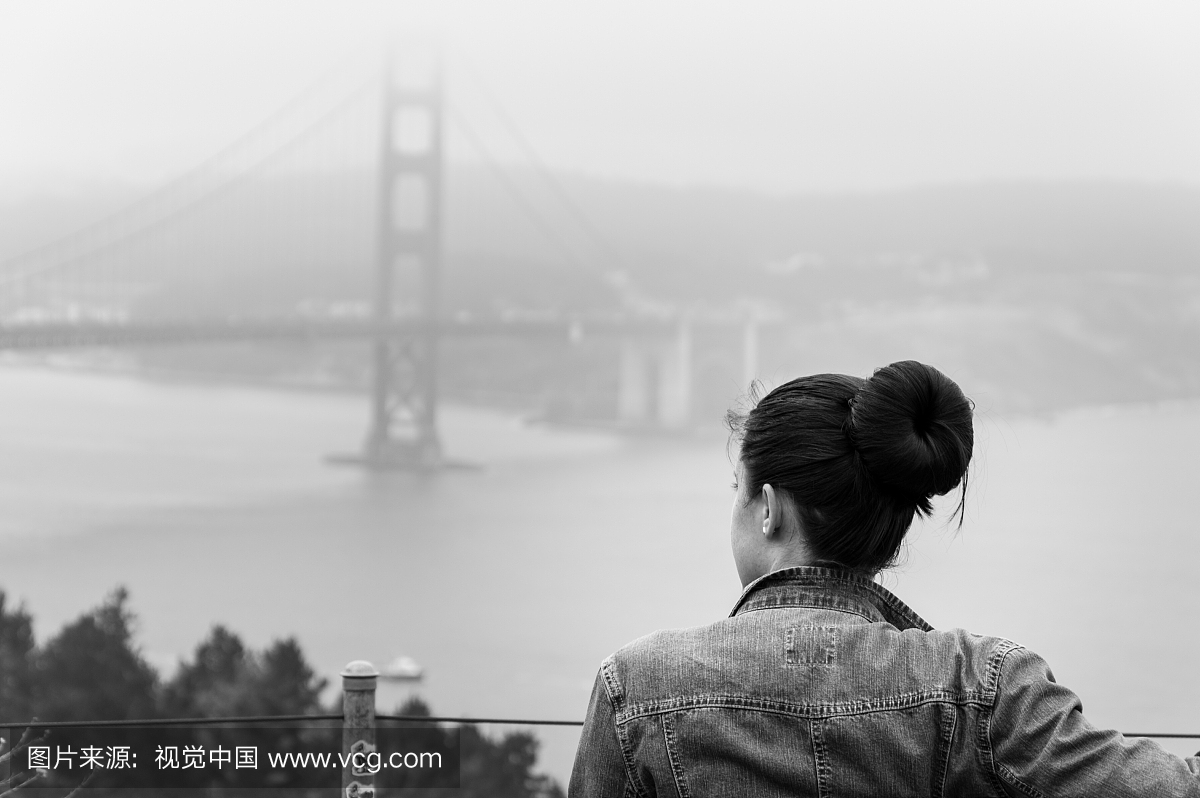 在恶魔天气中站在金门大桥的女人的后视图