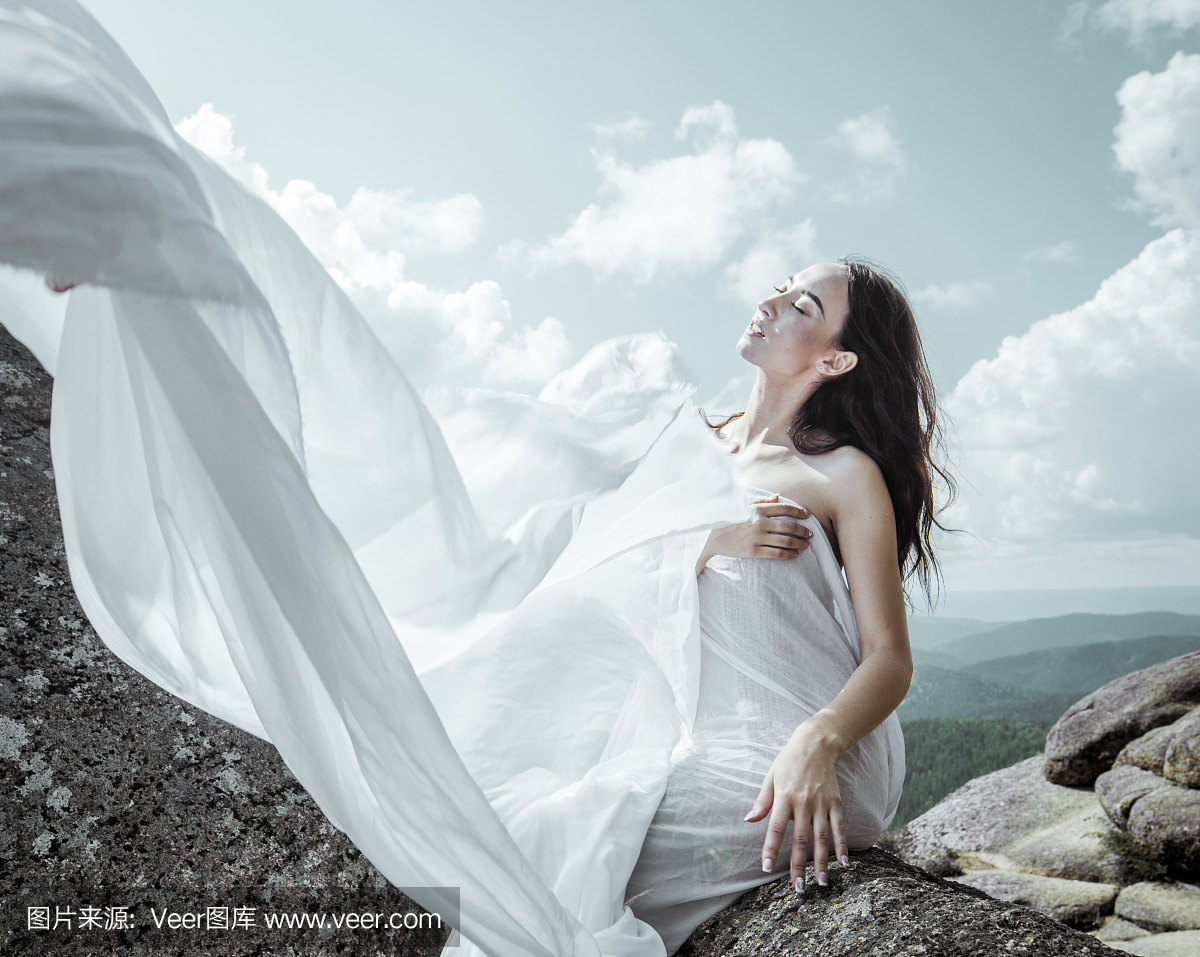 白色长布裙下的女孩在夏天的大岩石上