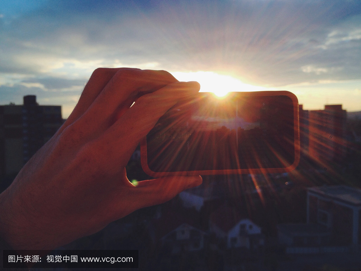 通过智能手机拍摄日落的照片的人的裁剪图像