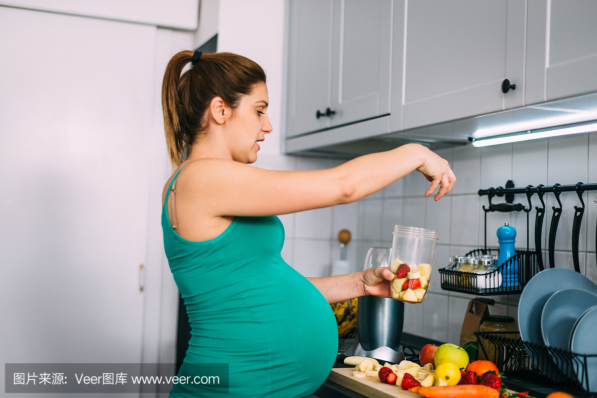 千禧年九个月孕妇在家里,在厨房里准备果汁