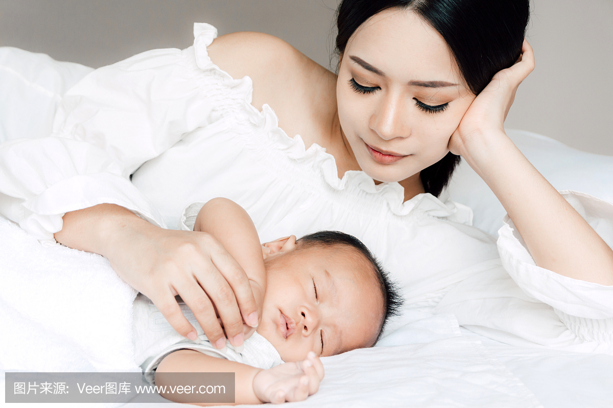 母亲抱着睡觉的婴儿手上白色的床上。家庭观念