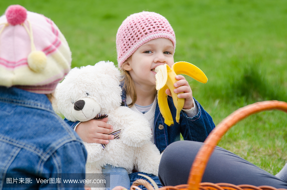 野餐的女孩吃一只香蕉,持熊