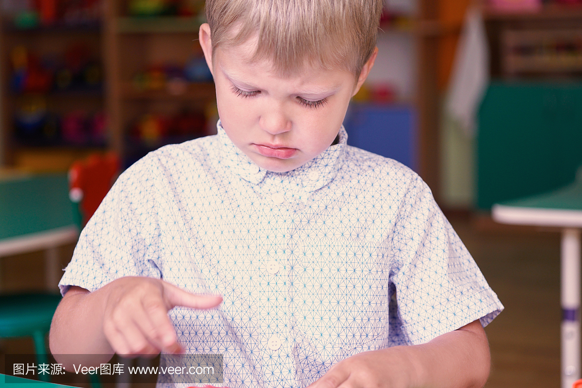 小沮丧的男孩玩在桌子上的彩色塑料砖在幼儿园