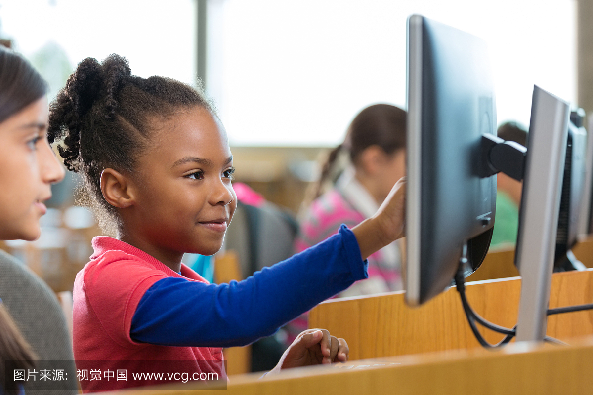 在学校图书馆使用电脑的可爱的小学年龄女孩