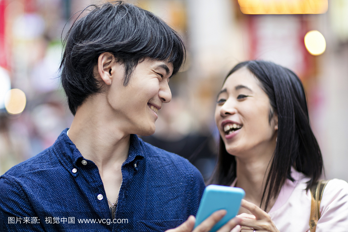 年轻的日本夫妇笑着看手机短信