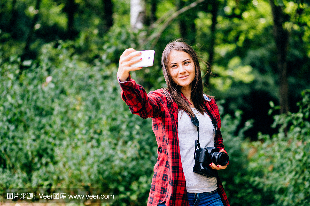 年轻漂亮的女孩穿格子衬衫采取与她的手机拍照