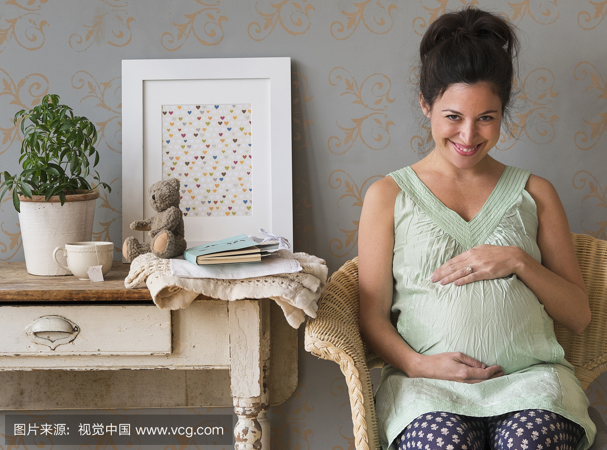 美国,新泽西州,孕妇坐在椅子上触摸腹部微笑