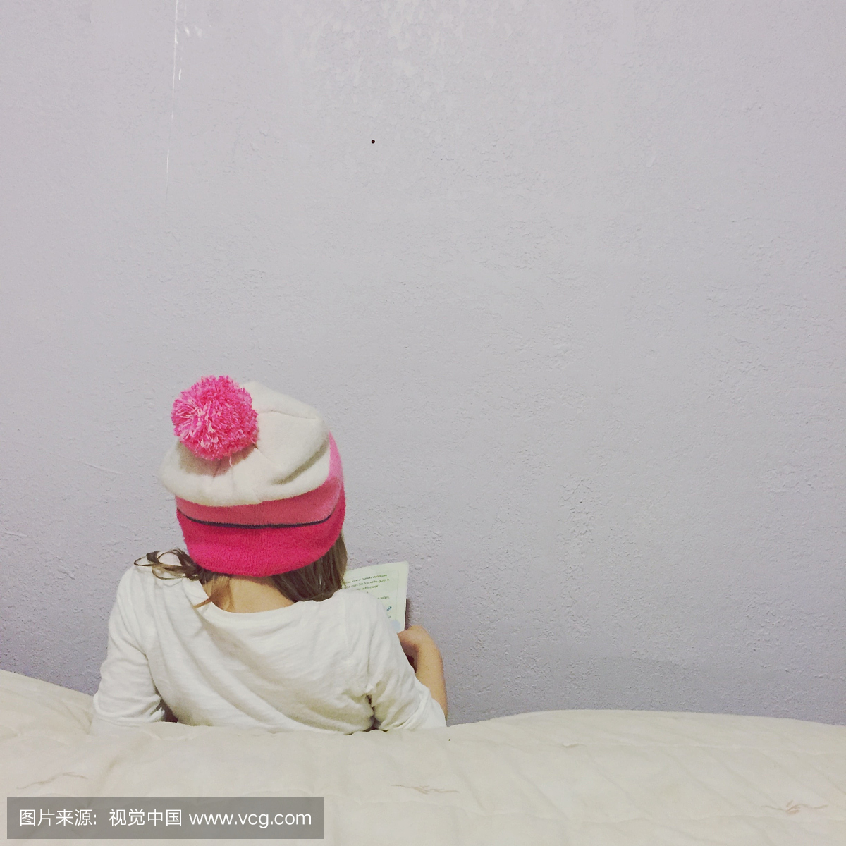 女孩的后视图编织帽子阅读书墙壁