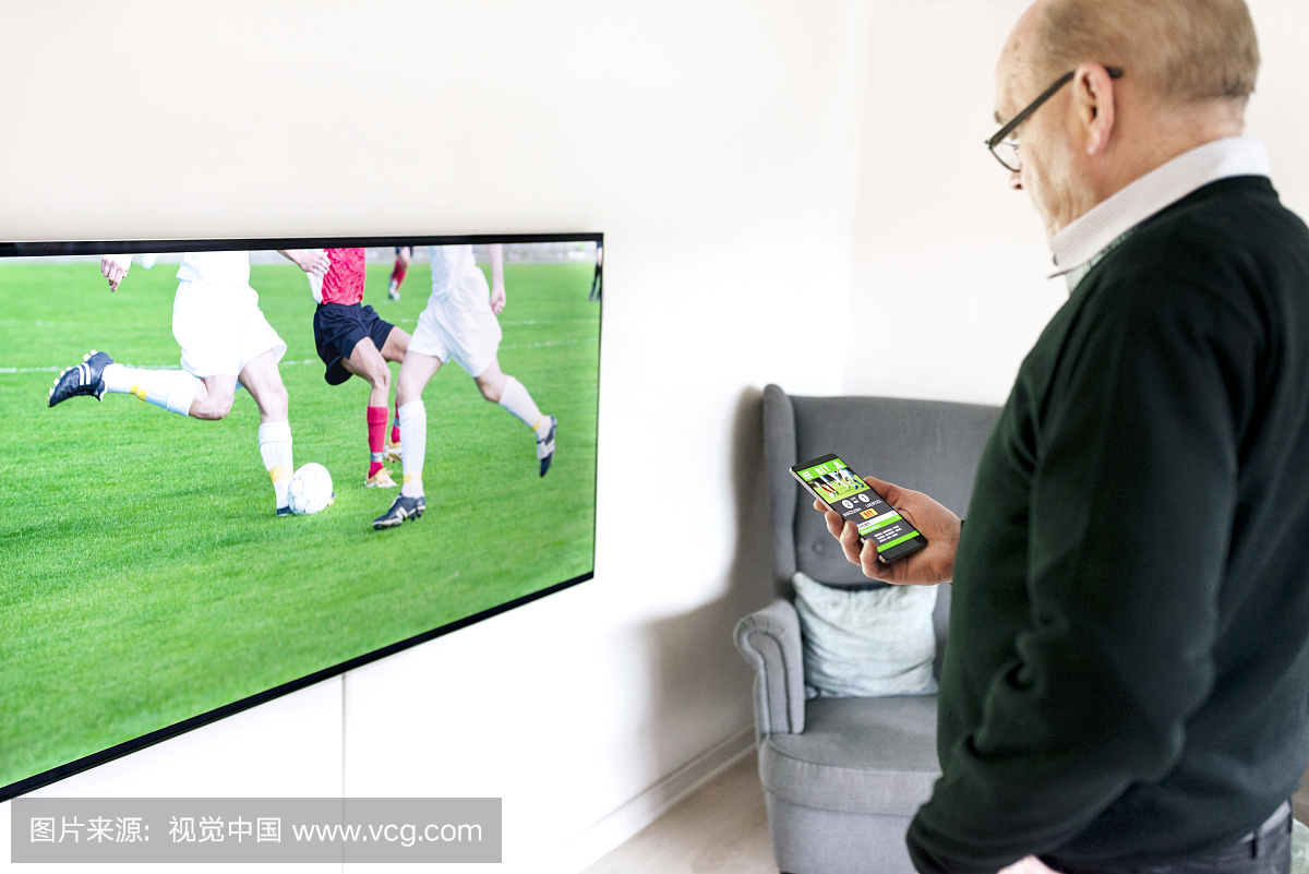 男子在手机上使用应用程序在电视上下注足球比赛