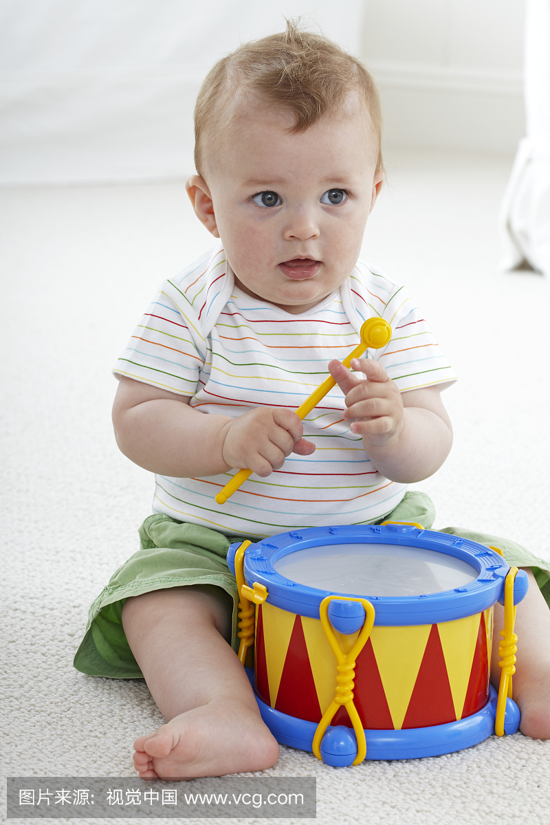 小男孩(9个月)坐在地板上玩玩具鼓