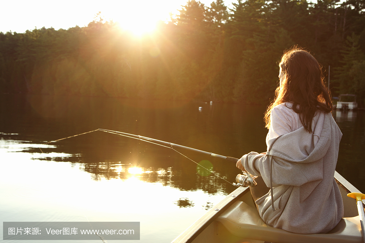 在日出时从独木舟钓鱼的女孩
