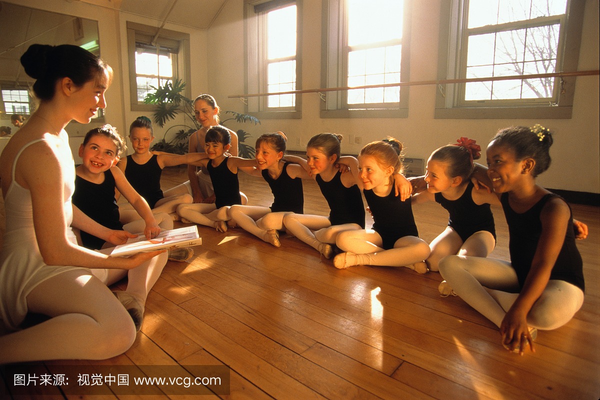 芭蕾舞学生(6-8)坐在课堂上,老师拿书打开书