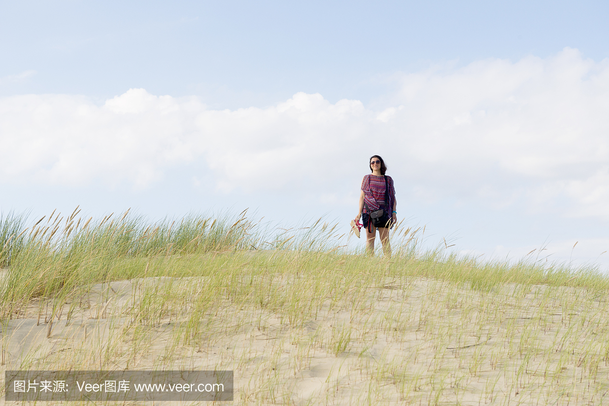 年轻女子在长满草的海滩沙丘上摆姿势