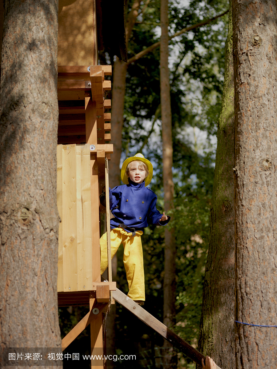 男孩(4-5)穿着消防员的服装站在树屋里