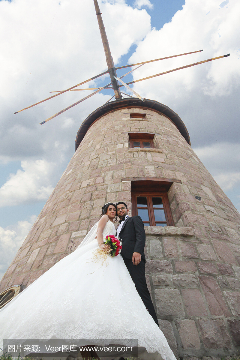 新娘和新郎在石头风车附近摆姿势。爱和婚礼概