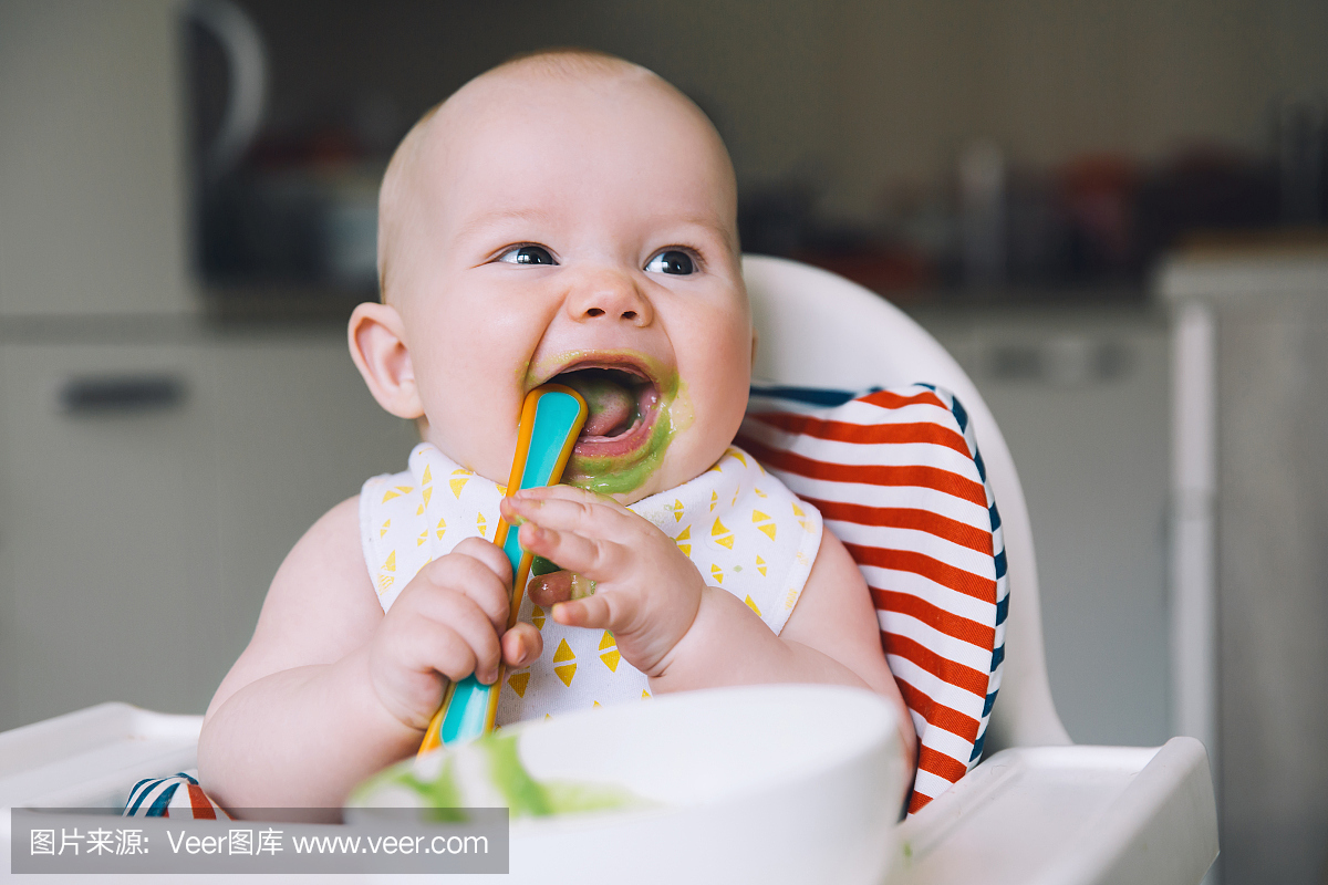 喂养。凌乱的微笑宝贝用高椅子上的勺子吃。宝