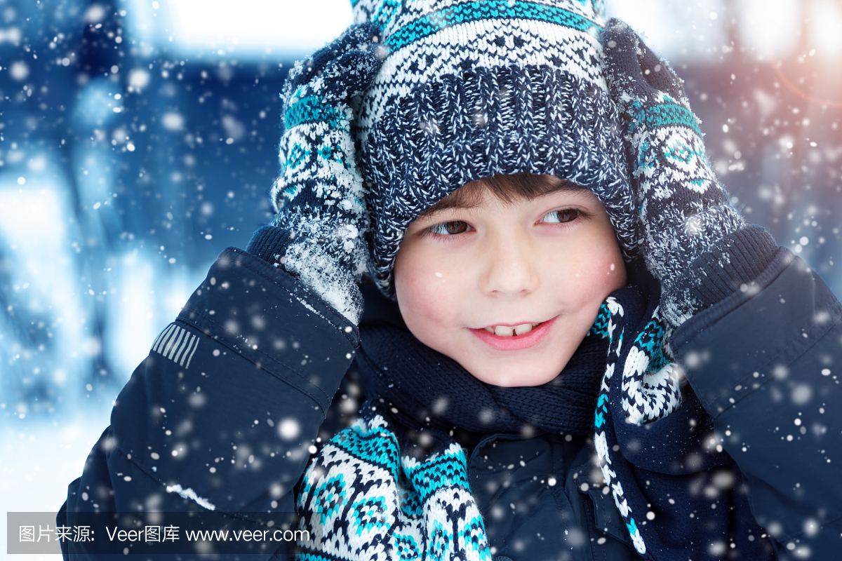 男孩在针织的帽子,手套和围巾在户外在降雪