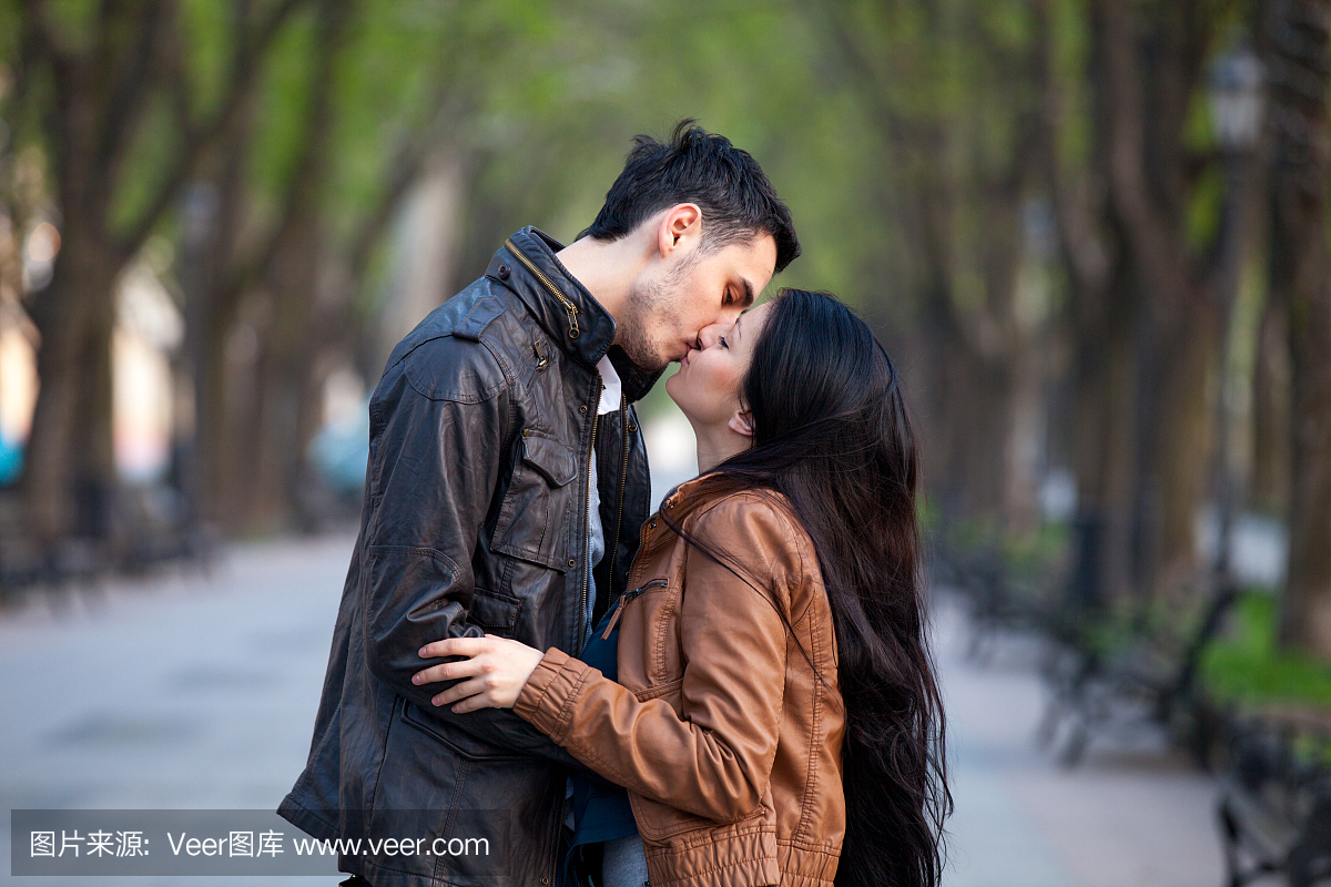 可爱的情侣亲吻和拥抱在美好的公园背景照片