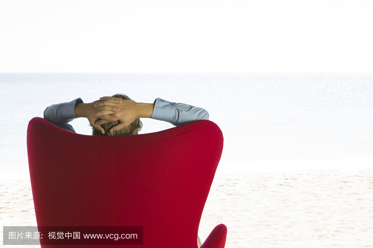 坐在椅子上的年轻人用手在头后面,后视图